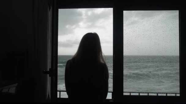 La ragazza guarda il mare infuria dalla finestra. Una donna sta guardando la tempesta. Silhouette di una donna alla finestra. Mare burrascoso. Grandi onde. Tempo piovoso ventoso. Veduta del drammatico . — Video Stock