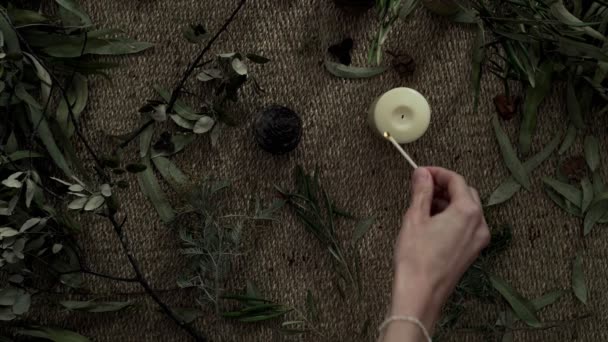 Flatlay με ψάθινο χαλί, ξηρά φυτά, και ένα κερί. Κοντινό πλάνο των γυναικείων χεριών που ανάβουν ένα κερί. Βραδινές τελετές. Φυσικά χρώματα. Οικολογική αισθητική. Ανθοπωλείο. — Αρχείο Βίντεο