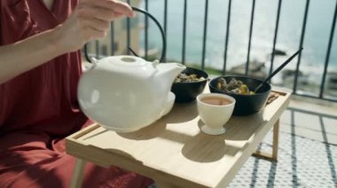 Terasta kahvaltı var. Güneşli terasta piknik. Sağlıklı kahvaltı. Kız fincana çay dolduruyor. Fındıklı, meyveli ve ballı lezzetli sağlıklı yulaf lapası. Sabah çayı. Eko ürünler. Diyet kahvaltı..