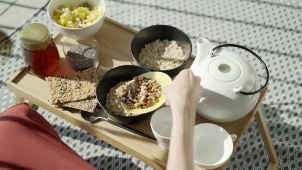 Petit déjeuner sur la terrasse. Pique-nique sur la terrasse ensoleillée. Petit déjeuner sain. La fille ajoute des noix à la farine d'avoine. Savoureux porridge sain avec des noix, des fruits et du miel. Thé du matin. Produits écologiques. Petit déjeuner diététique . — Video