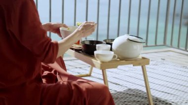 Terasta kahvaltı var. Güneşli terasta piknik. Sağlıklı kahvaltı. Kız yulaf ezmesine meyve ekliyor. Fındıklı, meyveli ve ballı lezzetli sağlıklı yulaf lapası. Sabah çayı. Eko ürünler. Diyet kahvaltı..