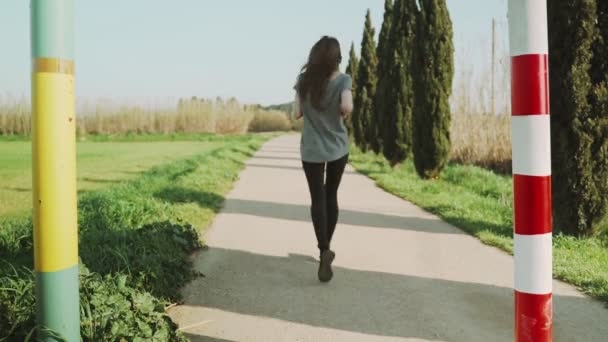 若い運動選手の女性は春の朝にジョギング。ヒノキの木や緑のフィールドの間の道路に沿ってジョギング。アウトドアスポーツ。健康的なライフスタイル。美しい田園風景。春の色。走る. — ストック動画