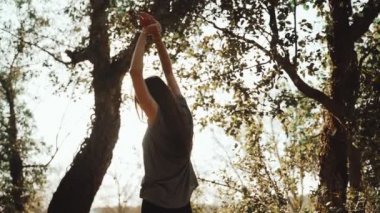 Genç bir atletik kadın koşudan önce esniyor. Parkta ağaçların arasında koşuya hazırlanıyorum. Açık hava sporları. Sağlıklı bir yaşam tarzı. Güzel kırsal manzara. Bahar renkleri. Altın ışık. Çalışıyor.