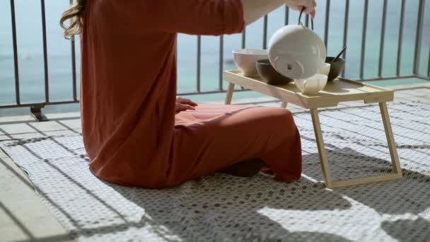 Colazione sulla terrazza. Picnic sulla terrazza soleggiata. Colazione sana. La ragazza versa il tè in una tazza. Saporito porridge sano con noci, frutta e miele. Tè mattutino. Prodotti ecologici. Colazione dietetica . — Video Stock