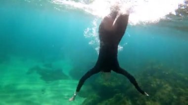 Siyah neopren takım elbiseli bir kız su altında yüzüyor. Sualtı çatışması. Triatlon. Güneş ışınları zümrüt sularda. Sprey ve güneş denizin dibinde parlıyor. Açık denizde yüzmek.. 