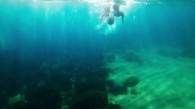 Siyah neopren takım elbiseli bir adam su altında yüzüyor. Sualtı çatışması. Triatlon. Güneş ışınları zümrüt sularda. Sprey ve güneş denizin dibinde parlıyor. Açık denizde yüzmek.. 