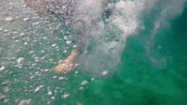 Siyah neopren takım elbiseli bir adam su altında yüzüyor. Sualtı çatışması. Triatlon. Güneş ışınları zümrüt sularda. Sprey ve güneş denizin dibinde parlıyor. Açık denizde yüzmek.. 