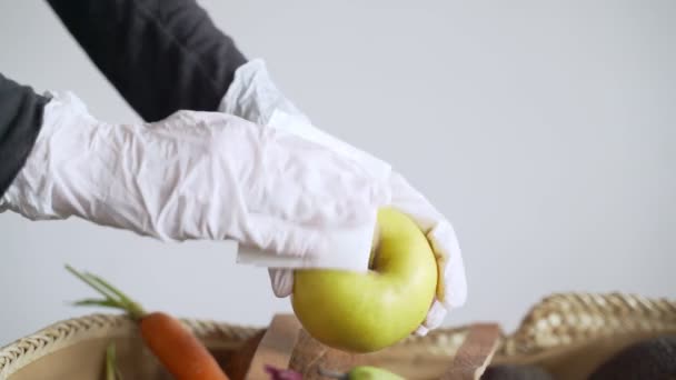 O femeie cu mănuși din latex ia un măr verde dintr-un coș alimentar și îl șterge cu un dezinfectant. Dezinfectare. Precauții pentru epidemia de virus. Carantină coronavirus. Cumpărături sigure . — Videoclip de stoc