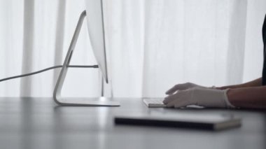Bir adam evden çalışır. Lateks eldivenli bir adam klavyeye yazı yazıp defterini kontrol ediyor. Merkez ofis. Virüs salgını için önlemler. Coronavirus karantinası. Evde kal. Salgın. 