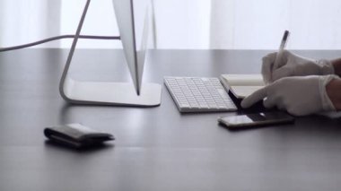 Bir adam evden çalışır. Lateks eldivenli bir adam not defterine not alır. Merkez ofis. Virüs salgını için önlemler. Coronavirus karantinası. Evde kal. Evden çalışıyorum. Salgın. Kendine dikkat et..
