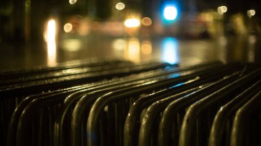 Şehirde yağmurlu bir akşam. Metal bir çitin üzerine parlak yağmur damlaları. Arka planda çok renkli şehir ışıkları var. Yaratıcı akşam ışıkları ve bulanık gölgeler. Alacakaranlık havası. Kapat..