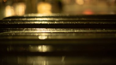 Şehirde yağmurlu bir akşam. Metal bir çitin üzerine parlak yağmur damlaları. Arka planda çok renkli şehir ışıkları var. Yaratıcı akşam ışıkları ve bulanık gölgeler. Alacakaranlık havası. Kapat..