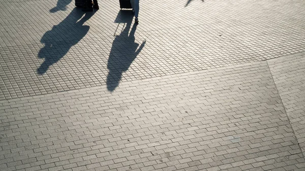 Urban scene. Silhouettes of people and shadows on the earth. Shadows on the street tiles. Bright sun and contrasting shadows. City walks. Urban lifestyle.