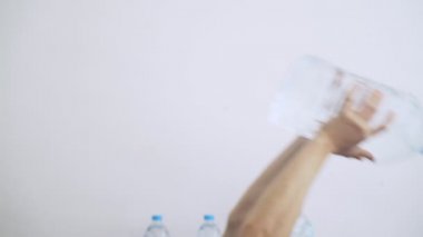 Evde spor var. Evde idman yapıyorum. Adam, plastik su şişesini bir su kemeri gibi kullanarak egzersiz yapıyor. El egzersizleri. Doğaçlama aletli spor. Evde kal. Karantina sırasında formda kalın. Pazılar, trisepsler. 