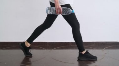 Evde spor var. Evde idman yapıyorum. Kettlebell gibi plastik su şişesiyle egzersiz yapan bir kız. Kettlebell çömeldi. Doğaçlama aletli spor. Evde kal. Karantina sırasında formda kalın. Bacaklar, kalçalar.