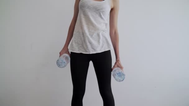 Deporte en casa. Entrenamiento en casa. Chica haciendo ejercicios usando botellas de agua de plástico como mancuernas. Ejercicios. Deporte con herramientas improvisadas. Quédate en casa. Manténgase en forma durante la cuarentena. Bíceps, tríceps — Vídeo de stock