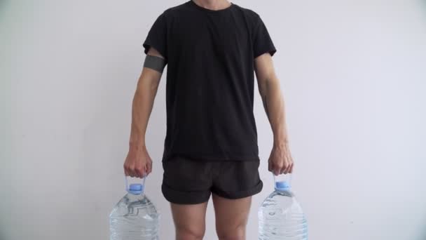 Deporte en casa. Entrenamiento en casa. Hombre haciendo ejercicios usando una botella de agua plástica como una campana de agua. Ejercicios. Deporte con herramientas improvisadas. Quédate en casa. Manténgase en forma durante la cuarentena. Biceps, tríceps — Vídeo de stock