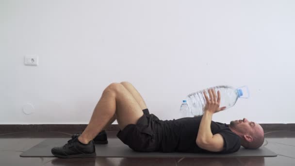 Deporte en casa. Entrenamiento en casa. Hombre haciendo ejercicios usando una botella de agua plástica como una campana de agua. Ejercicios. Deporte con herramientas improvisadas. Quédate en casa. Manténgase en forma durante la cuarentena. Biceps, tríceps — Vídeos de Stock