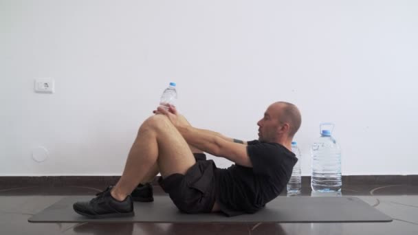 Deporte en casa. Entrenamiento en casa. Hombre haciendo ejercicios usando una botella de agua plástica como una mancuerna. Ejercicios abdominales. Deporte con herramientas improvisadas. Quédate en casa. Manténgase en forma durante la cuarentena. Prensa — Vídeo de stock