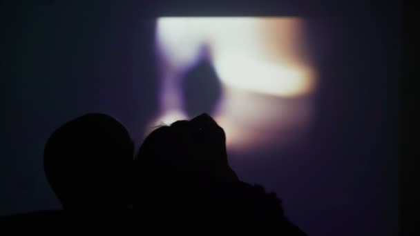 Silueta de una pareja enamorada en el fondo de la pantalla de la pared. Una pareja está viendo una película en un proyector. Qué hacer en casa. Viendo una película en casa. Quédate en casa. Diviértete en casa . — Vídeos de Stock