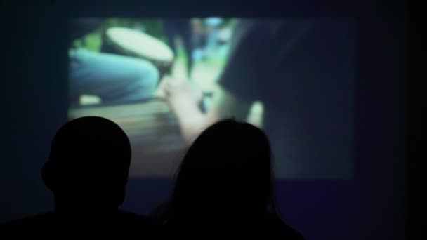 Silueta de una pareja enamorada en el fondo de la pantalla de la pared. Una pareja está viendo una película en un proyector. Qué hacer en casa. Viendo una película en casa. Quédate en casa. Diviértete en casa . — Vídeos de Stock