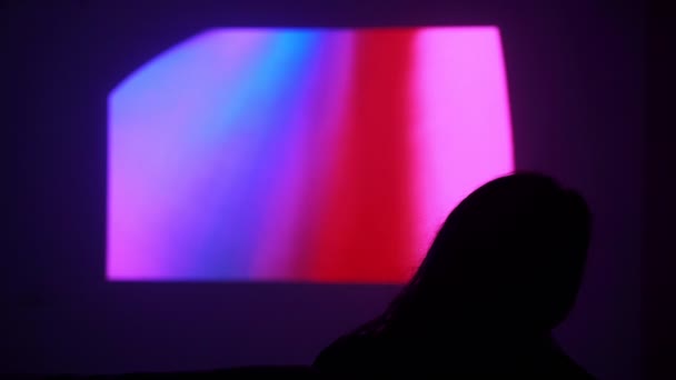 Silueta de una chica en el fondo de la pantalla en la pared. La mujer está viendo una película en un proyector. Qué hacer en casa. Viendo una película en casa. Quédate en casa. Diviértete en casa. Cuarentena . — Vídeos de Stock