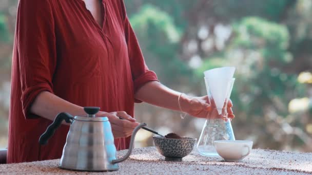 Dělám doma speciální kávu. Filtrovat kávu na terase s výhledem. Dívka nalije kávu do filtru. Zůstaň doma. Domovská baristka. Speciální kávové nástroje. Zůstaň v bezpečí. — Stock video