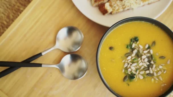 Närbild av en trälåda med lunch serveras. Smaklig pumpa soppa med ost krutonger. Friska livsmedel. Ljusorange soppa med pumpafrön i en svart skål. Hälsosam kost. Smaklig vegetarisk mat. — Stockvideo