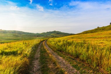Yolun karşısında alan tepeler arasında.