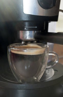 The coffee maker. Close shot. Coffee in a double-walled glass cup. Coffee is poured from a coffee machine in the morning
