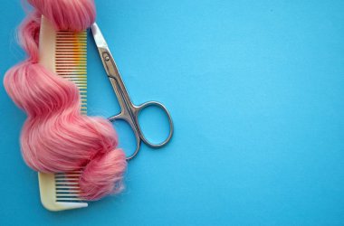 Parlak pembe saç ve makas bukleleriyle tarağın en üst görüntüsü. Parlak mavi bir arka planda. Güzellik salonu konsepti, kuaför..