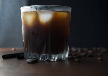 Buzlu kahve, bir bardak soğuk kahve. Koyu çikolata ve kahve çekirdeği. Yan görünüm, koyu arkaplan.