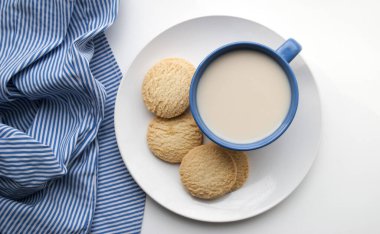 Tabağında kurabiyeler olan bir fincan kahve ve beyaz arka planda mavi peçete.