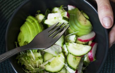 Avokado, salatalık, turp, mikro keten ve roka yeşili vejetaryen salatası. Sağlıklı yemek, öğle yemeği molası. Kadın eli ve çatal ve salata yakın plan. Sağlıklı yeme kavramı.