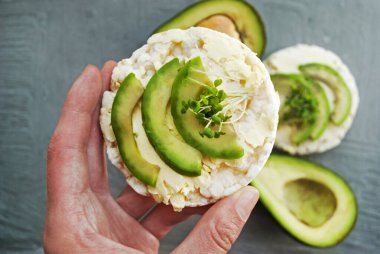 Glütensiz pirinç keki, kraker, avokado ve mikroyeşil. Kadın eli bir sandviç alır. Vejetaryen kahvaltısı avokado pirinç keki.