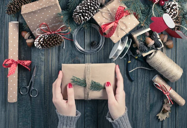 Regalos y pergaminos empacados, ramas de abeto y herramientas en la mesa de madera en mal estado. Lugar de trabajo para la preparación de decoraciones hechas a mano año nuevo . — Foto de Stock