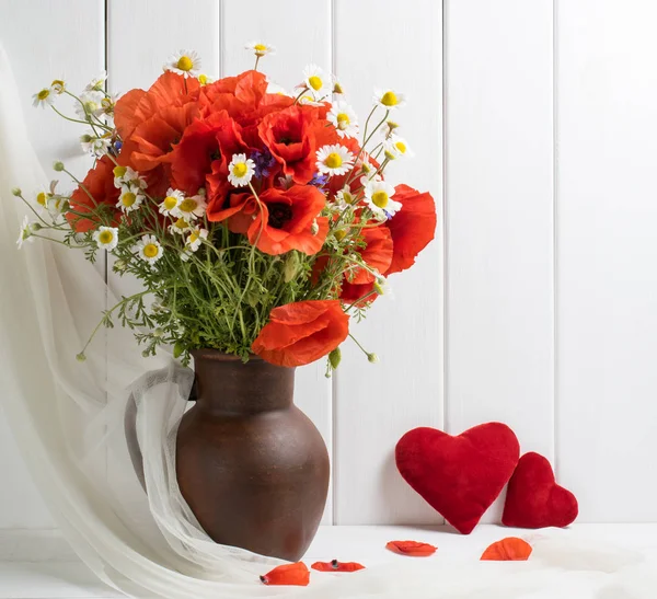 Amapolas rojas en jarra de arcilla y dos corazones en tablones de madera backgrou —  Fotos de Stock