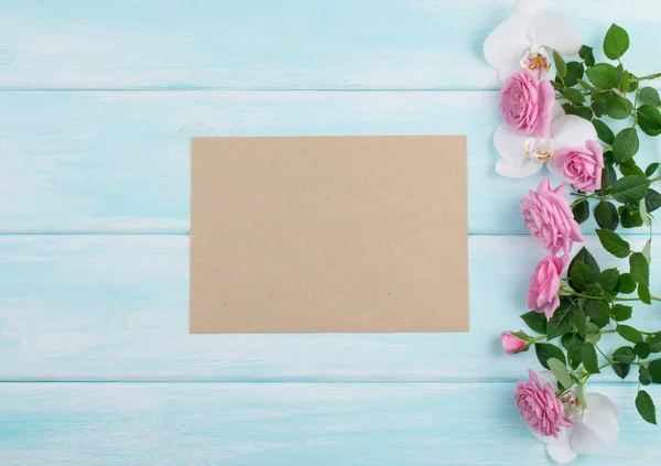 Fundo de madeira com rosas e orquídea e papel ecológico vazio — Fotografia de Stock