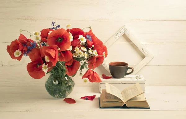 Buquê de papoilas vermelhas em vaso redondo, livro aberto, xícara de chá — Fotografia de Stock
