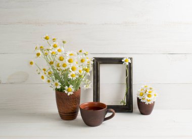 Fincan çay ve fotoğraf çerçevesi ile kil vazoda papatya buketi