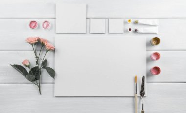 Çalışma alanı ile tuval, Boya fırçaları, palet bıçağı, gül ve boyalar ahşap kurullarında. Üstten Görünüm. Düz tasarım.