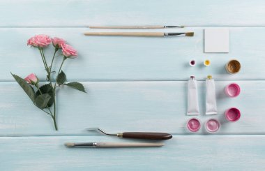 Boya fırçaları, palet bıçağı, gül ve boyalar ahşap kurullarında iş yeri. Üstten Görünüm. Düz tasarım.