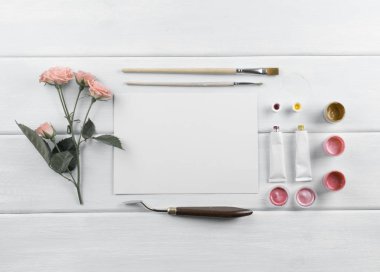 Çalışma alanı ile tuval, Boya fırçaları, palet bıçağı, gül ve boyalar ahşap kurullarında. Üstten Görünüm. Düz tasarım.