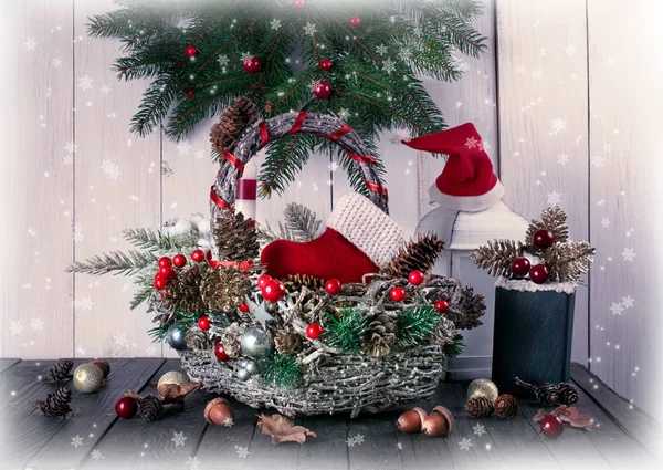 Kerst achtergrond met mand, rode Kerstman laars en hoed, witte lantaarn, dennenboom, doos, kegels en eikels op shabby houten oude tafel — Stockfoto