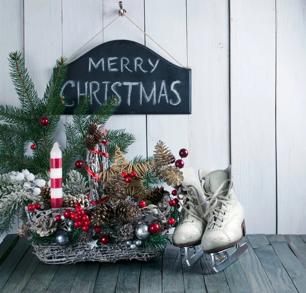 Feliz Navidad fondo con cesta, patines para patinaje artístico, abeto sobre tabla vieja de madera de mala calidad, pizarra con inscripción en pared blanca —  Fotos de Stock