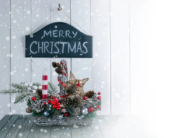 Merry Christmas background with wicker basket, fir tree on shabby wooden old table, blackboard with inscription on white wall