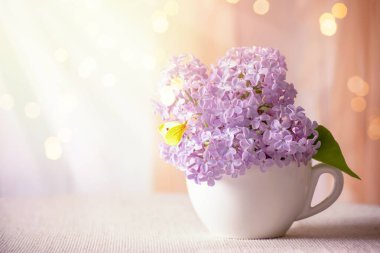 İçi mor leylaklarla dolu. Çay fincanında çiçek açıyor. Sarı kelebek, yumuşak sabah ışığında romantik bahar evi dekorasyonu, parlak, ışıldayan bokeh, şırıngayla dekore edilen ev.