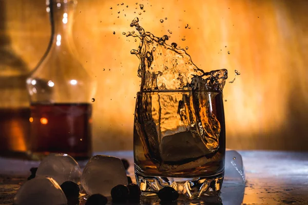 Splash of cold ice in glass of whiskey isolated on a light background