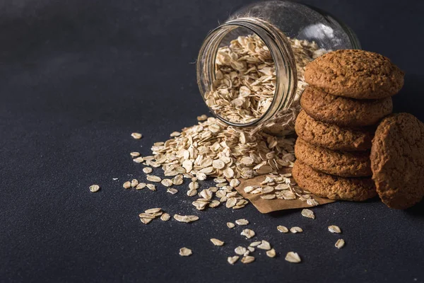 Şeffaf cam kavanozdaki lezzetli yulaf ezmesi ve koyu arkaplanda yulaf ezmeli kurabiye.