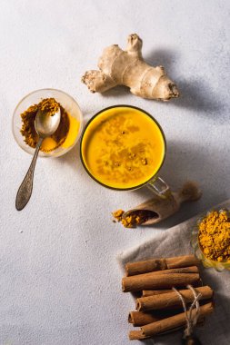 Beyaz zemin üzerinde altın zerdeçal sütü ve baharatlı tarçın ve malzemeler.